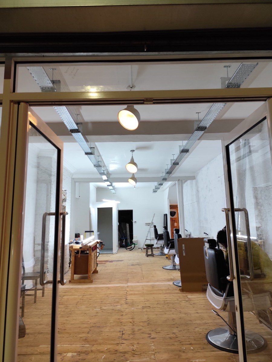 A barbershop fit-out in East London mid-installation, galvanised cable containment and track lighting fitted above the chairs by Hi Elec-Tech Solutions.
